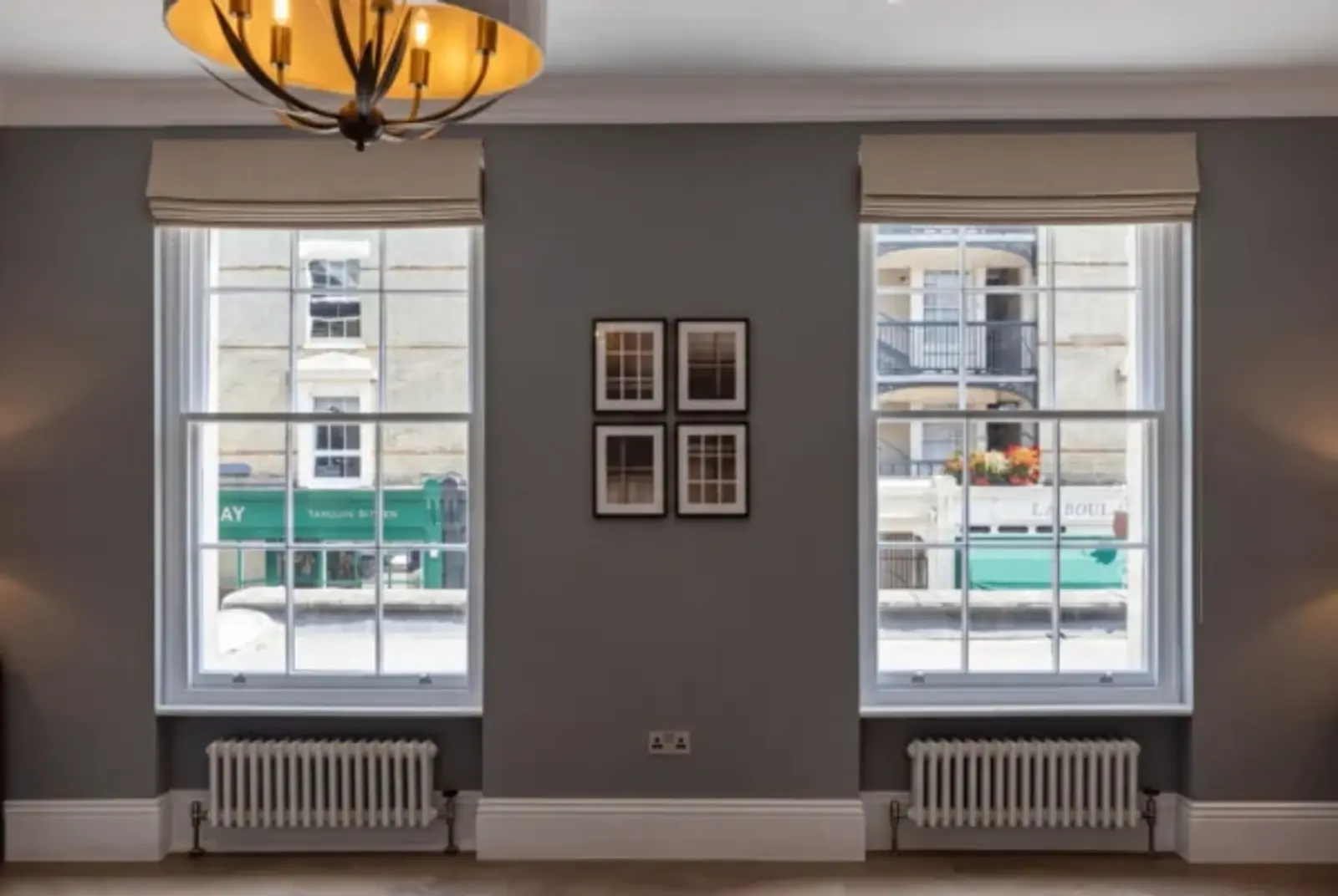 Pair of tall sash windows in a period room with taupe blinds and a street view