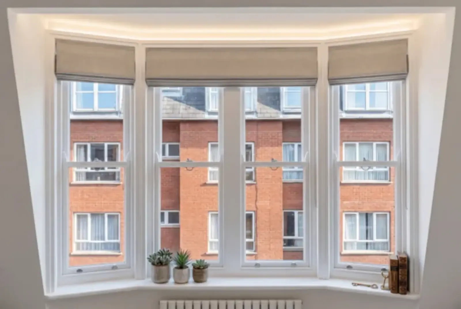 Curved bay window with four white-framed panes, blinds and terracotta rooftops beyond