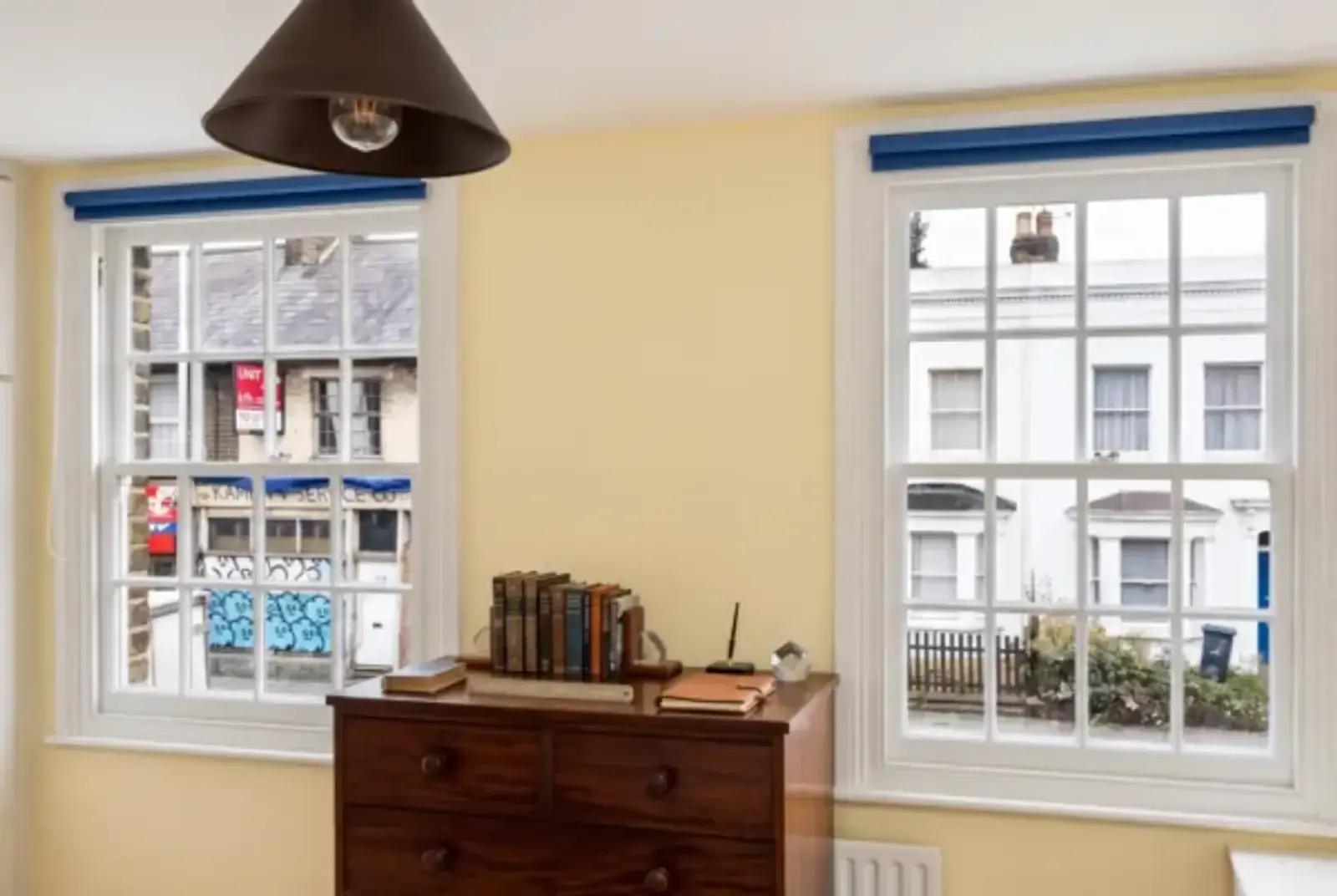 Warm study with two white-framed sash windows, blue blinds and a wooden chest