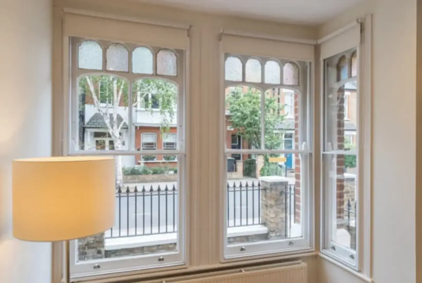 Period bay window with decorative arched panes, roller blinds and a tree-lined street view