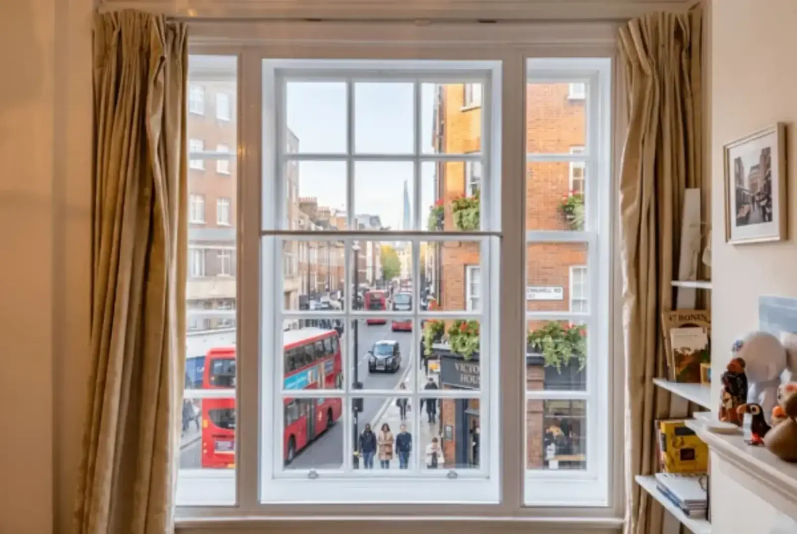 Period sash window overlooking a lively London street with red buses and terraced buildings