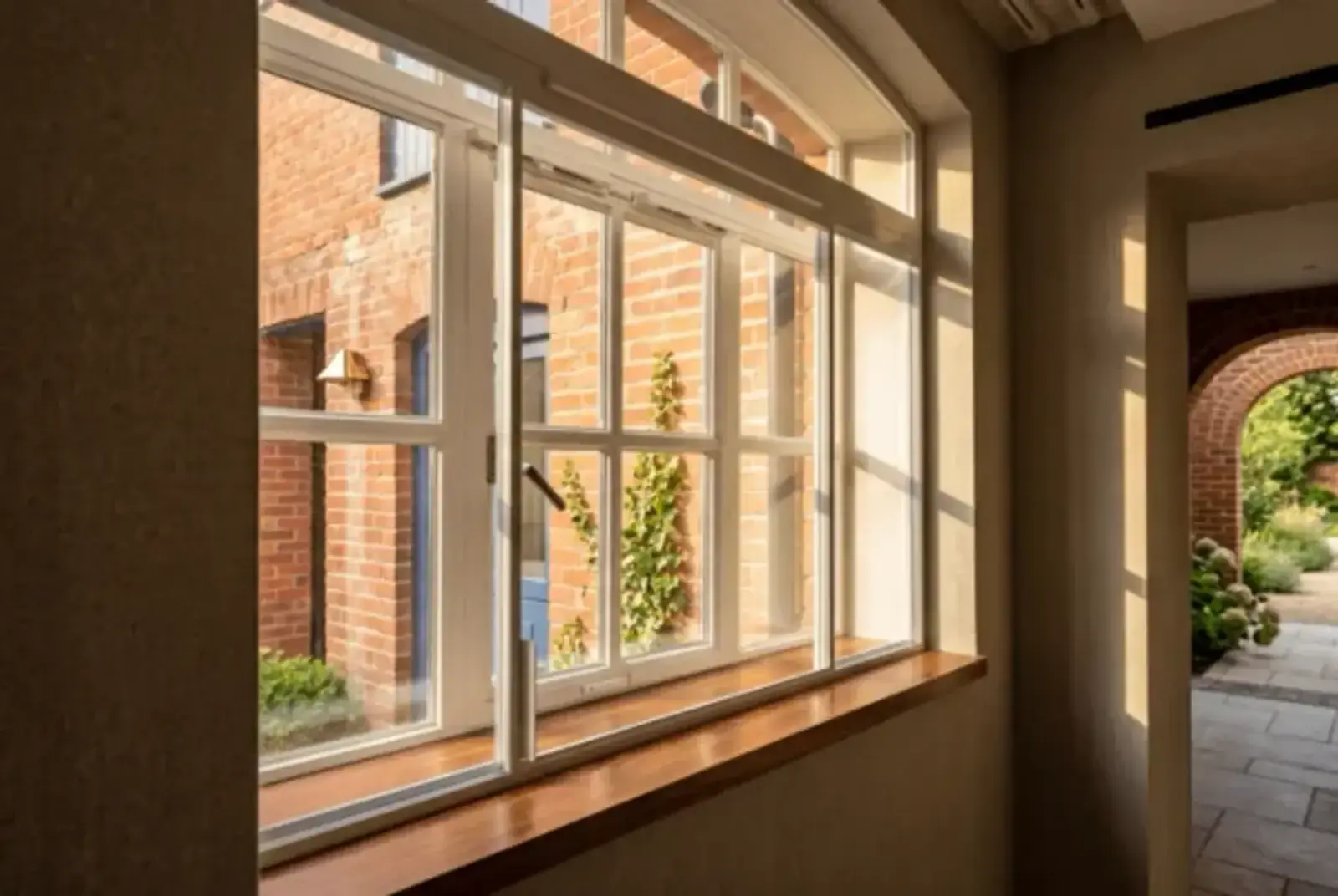 Slim white secondary glazing fitted across an interior passage with a brick courtyard beyond