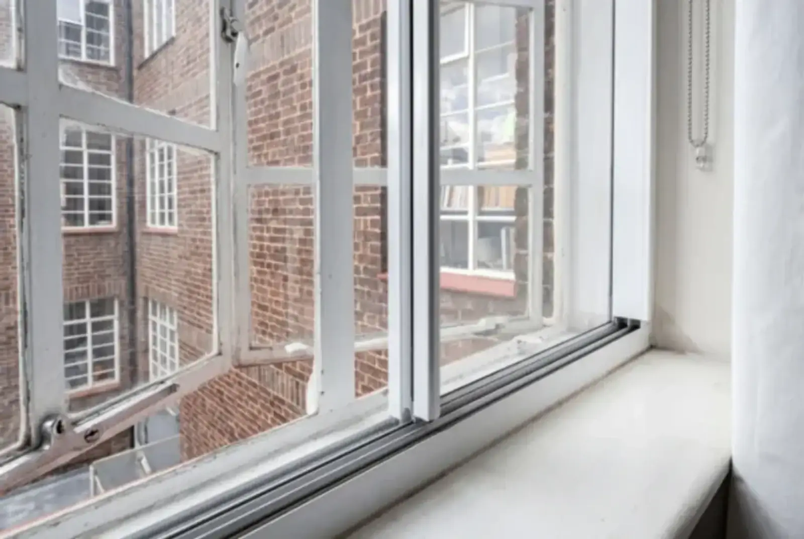 Close view of slim secondary glazing fitted inside a period window beside a brick courtyard