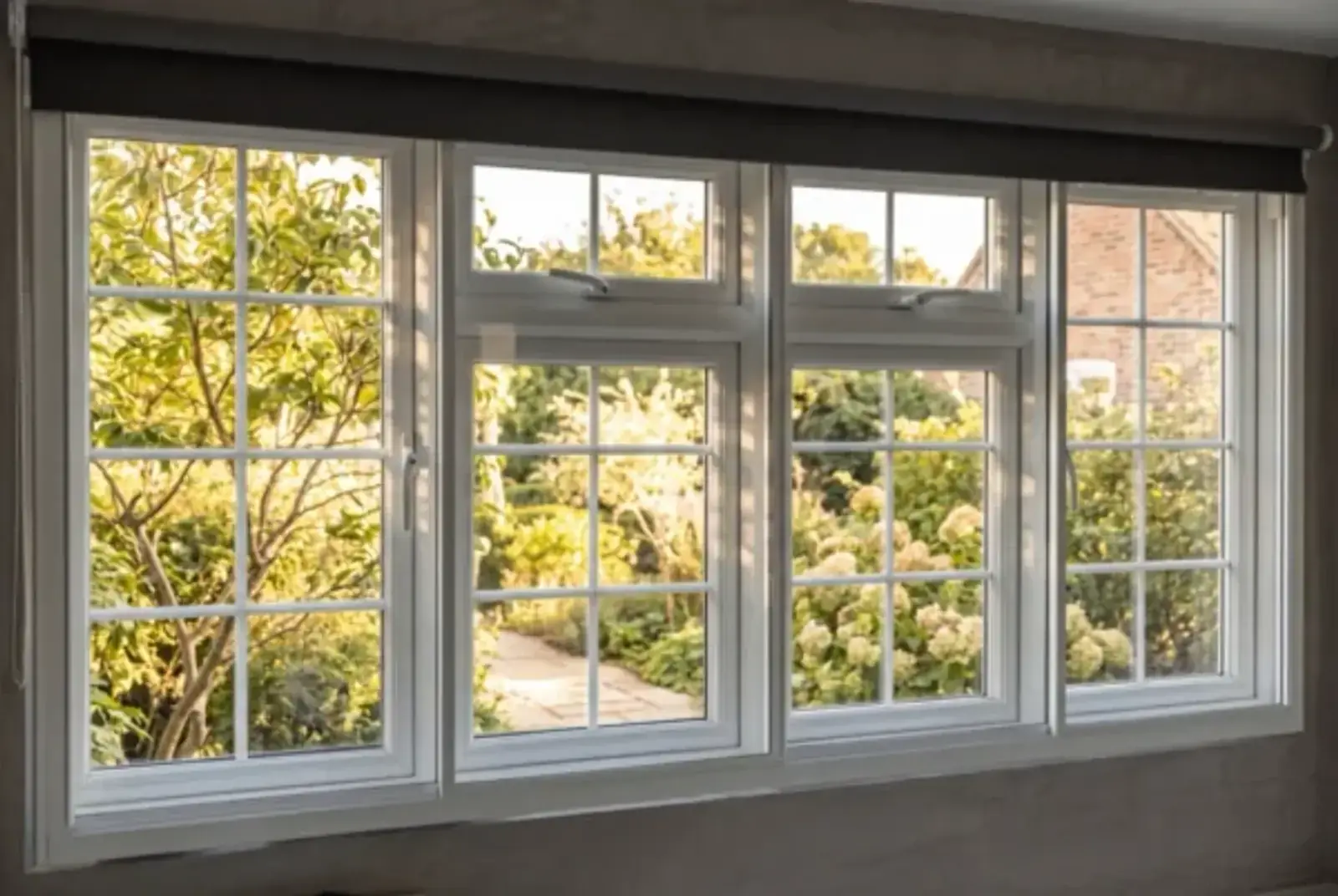 Long run of white-framed windows opening onto a green garden in warm evening light